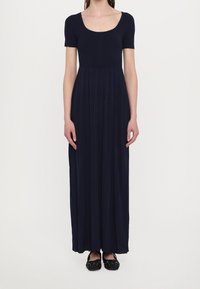 Marineblaue Maxikleid mit kurzen Ärmeln, geripptem Oberteil und plissiertem Rock. Kombiniert mit schwarzen flachen Schuhen mit dekorativen Akzenten.