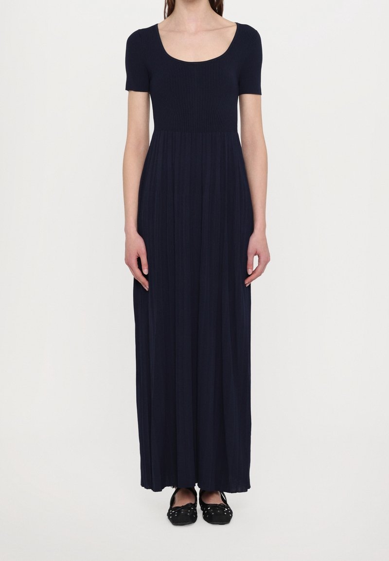 Marineblaue Maxikleid mit kurzen Ärmeln, geripptem Oberteil und plissiertem Rock. Kombiniert mit schwarzen flachen Schuhen mit dekorativen Akzenten.