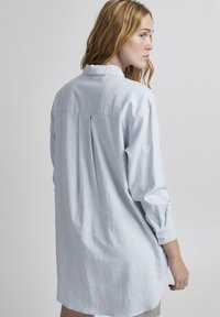 Chemise à manches longues bleu clair en tissu doux. Dispose d'un poignet à boutons et d'un pli dans le dos, avec une coupe décontractée et surdimensionnée.
