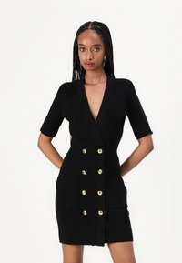 Μαύρο πλεκτό φόρεμα με βαθύ V ντεκολτέ, κοντά μανίκια, διπλό κούμπωμα με χρυσά κουμπιά και δύο μπροστινές τσέπες.