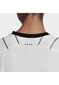 Primo piano del collo e della parte superiore della schiena di una persona che indossa una maglietta sportiva bianca con colletto nero e quattro stelle nere centrate sotto il colletto.