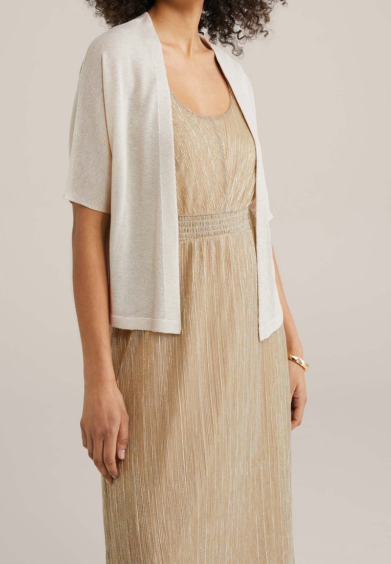 Lehké šálové bolerko s otevřeným předním dílem z lesklé krémové látky, doplněné zlatými plisovanými šaty. Krátké rukávy a volný střih.