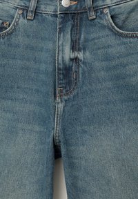 Jean en denim bleu avec bouton à l'avant, fermeture éclair, passants de ceinture et coutures orange visibles sur les poches et les coutures.