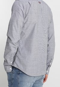 Šedá košile s knoflíky a vzorem, hladká na dotek, s dlouhými rukávy, bílými knoflíky a zaobleným spodním lemem.