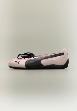 Chaussure plate Puma rose et noire avec des lacets noirs, montrant le profil latéral sur un fond neutre.