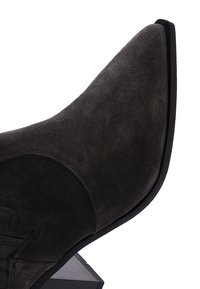Bottine en daim gris foncé avec un bout pointu et un talon noir épuré. Présente des accents de couture subtils sur le côté.