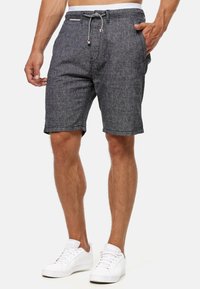 Shorts gris texturé avec un waistband à cordon de serrage, deux poches latérales et un revêtement blanc contrastant, associés à des baskets blanches.