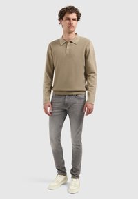 Beige Langarm-Polohemd mit strukturiertem Rippstoff, ausgestattet mit einer Knopfleiste mit drei Knöpfen, kombiniert mit grauen Slim-Fit-Jeans und weißen Sneakers.