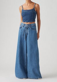 Denim crop top met vierkante halslijn en dunne bandjes, gecombineerd met wijde denim jeans met een strik taille, allemaal in een lichtblauwe tint.