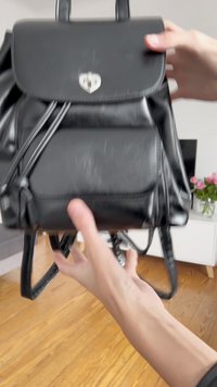 Schwarzer Leder-Rucksack mit Klappenverschluss, silberner herzförmiger Hardware, verstellbaren Trägern und strukturierten Oberflächen, die Gebrauchsspuren aufweist.