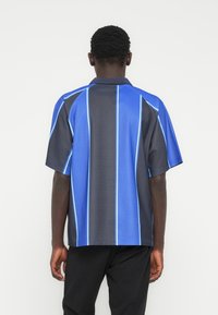 Κοντομάνικη πόλο μπλούζα με μπλε και σκουρόγκρι ύφασμα και κάθετες ανοιχτό μπλε ρίγες. Ομαλή υφή και άνετη εφαρμογή.