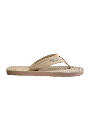 Sandalia beige tipo flip-flop con suela texturizada, tiras gruesas de tela y una pequeña etiqueta de marca en la correa lateral.