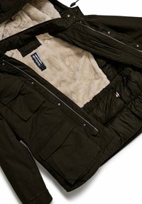 Donkergroene parka jas met een zachte beige fleece voering. Beschikt over ritsen, meerdere zakken en een trekkoord capuchon. Duurzaam materiaal.