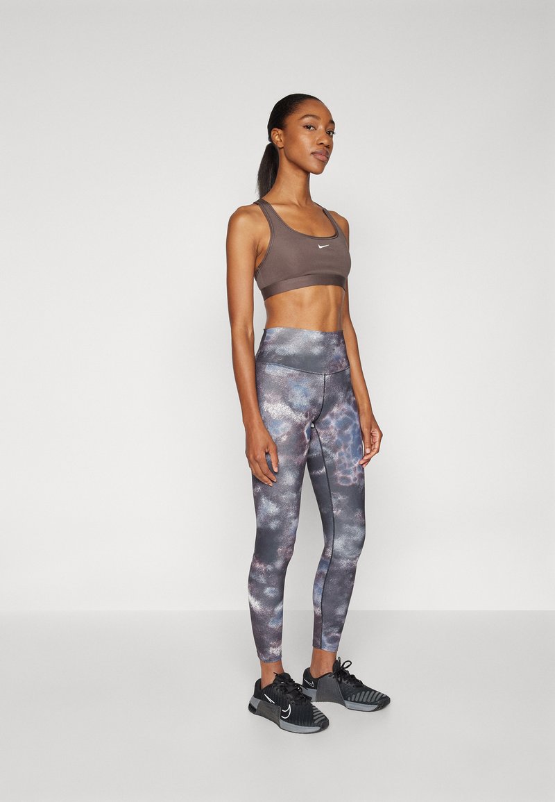 Soutien-gorge de sport en tissu marron, leggings taille haute avec un motif galaxie en bleu et gris, associés à des chaussures de sport noires.
