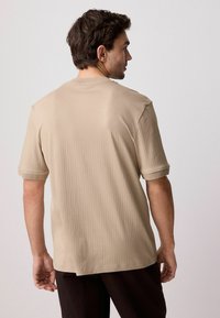 Beige ribbet t-shirt med kortærmer, featuring en rund halsudskæring og rullede ærmer, designet med en glat tekstur og afslappet pasform.