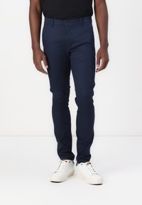 Tengerészkék, pamut keverékből készült, szabott nadrág, gombos záródással, oldal zsebekkel és slim fit fazonnal, fehér sportcipővel párosítva.