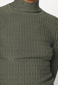Groene gebreide coltrui met een gestructureerd ruitpatroon. Getailleerd ontwerp met een hoge kraag en geribbelde randen. Zacht materiaal.