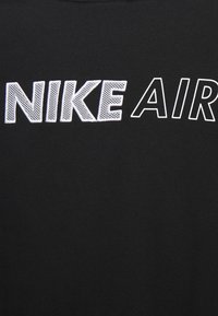 Svart t-shirt med texten "NIKE AIR" i fet vit och konturerad stil. Mjuk bomullstyg med en slät textur.