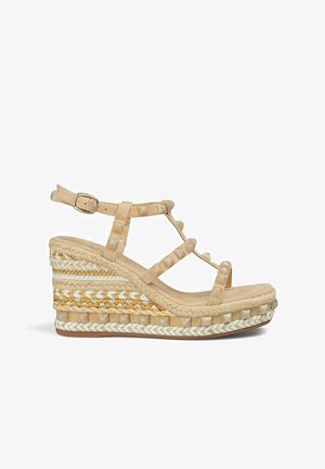 Sandale compensée en beige clair avec un design à lanières. Comprend des détails tissés sur la semelle et une fermeture à boucle. Matériaux doux et texturés.