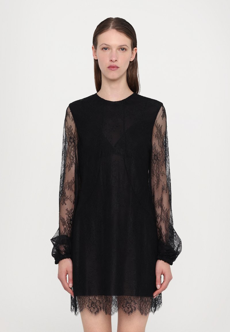 Rochie neagră din dantelă, cu mâneci lungi și transparente, decolteu rotund și un model floral texturat, cu o linie a tivului ușor evazată.
