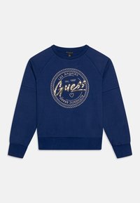 Marinblå sweatshirt med rund halsringning, raglanärmar och ribbad mudd. Centrerad grafik med "Guess" i glänsande guldtext inom en cirkulär ram.