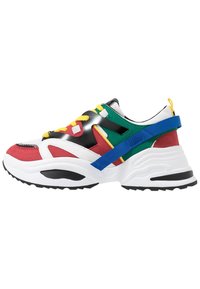 Zapatilla deportiva colorida con una combinación de materiales en rojo, verde y azul, parte superior de textil con detalles de plástico, suela gruesa blanca y cordones amarillos.