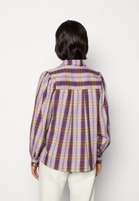 Purple and yellow checkered long-sleeve shirt with a high collar, gathered sleeves, and buttoned cuffs, made of a soft, textured fabric.