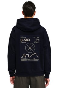 Granatowa bluza z kapturem z dużym nadrukiem na plecach, zawierającym białe napisy, grafikę gór oraz okrągły emblemat. Materiał bawełniany.