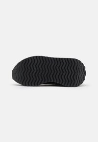 Schwarzer Sneaker-Sohle mit einem Zickzack-Profil und geprägtem Branding. Robustes Gummi-Material, das Traktion und Unterstützung bietet.