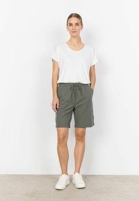 T-shirt blanc à col en V associé à un short vert foncé avec une taille élastique et un cordon de serrage. Le modèle porte des baskets blanches.