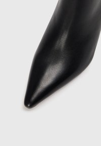 Černá kožená vysoká bota na jehlovém podpatku s špičatou špičkou, hladkým povrchem a lesklým finišem, zdůrazňující elegantní design a minimalistický styl.