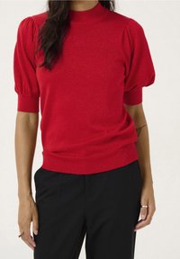 Czerwony sweter z krótkimi bufkami i prążkowanym dekoltem. Wykonany z błyszczącego materiału, o dopasowanym kroju i prążkowanym wykończeniu.
