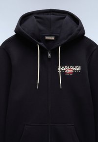 Sudadera con cremallera negra hecha de tela suave, que presenta un logo en blanco y rojo en el pecho, con cordones de color claro y bolsillos en la parte delantera.