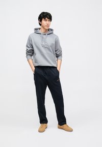 Halli kapuutsiga dressipluus paeladega ja kängurutaskuga, sobitatud tumesiniste dressipükstega; mõlemad pehmest kangast. Komplekti viimistlevad beežid tossud.