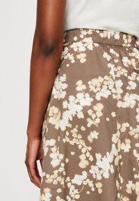 Gonna a fantasia floreale in tessuto marrone chiaro con fiori bianchi e pesca. Presenta una vita elastica e un design fluido.