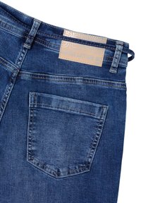 Vaqueros de denim en azul oscuro con una textura suave, que cuentan con un bolsillo trasero y una etiqueta de cuero marrón claro que dice "DENIM NUNCA ME DEJES IR."