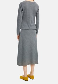 Szary dzianinowy sweter z długimi rękawami i okrągłym dekoltem, w zestawie ze szarym długim spódnicą. Żółte zamszowe buty wsuwane.