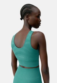 Teal sportieve crop top met een ribbeltextuur en een open rug, voorzien van ventilatiegaten en een glad ontwerp.