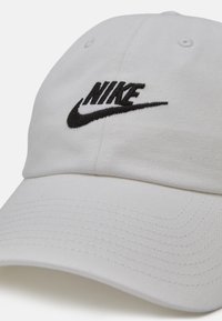 Balta medvilninė kepurė su juodu siuvinėtų "Nike" logotipu, su lenktu kraštu ir siuvinėtais detalėmis paviršiuje.
