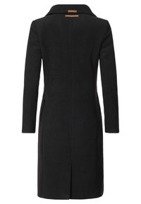 Cappotto lungo nero con taglio dritto, maniche lunghe, spacco posteriore e piccola etichetta marrone sotto il colletto.