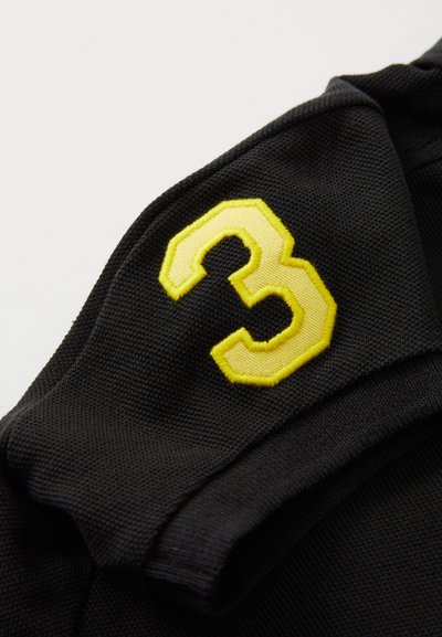 Tessuto nero con superficie texture presenta un grande numero "3" ricamato in giallo nella parte superiore.