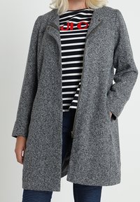 Abrigo gris con textura, de manga larga y cierre frontal con cremallera. Presenta bolsillos laterales y un corte holgado. Se lleva sobre una blusa a rayas.