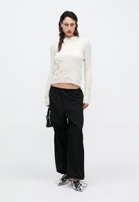 Pulover alb cropt cu dungi și tiv destrămat, asortat cu pantaloni negri cu picioare largi. Pantofi argintii cu vârf ascuțit și o geantă neagră completează ținuta.