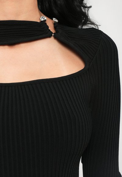 Black ribbed top featuring a square neckline, unique draped detailing, and embellishments at the collar. Soft fabric with a textured finish.