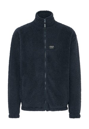 Chaqueta de forro polar en azul marino oscuro, con cuello alto, cierre de cremallera completo, superficie texturizada y una pequeña etiqueta de marca negra en el pecho.