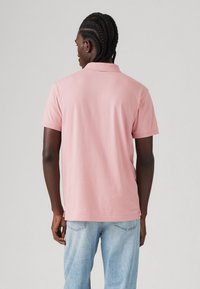 Polo shirt rose clair à manches courtes, avec un col classique et une coupe décontractée, associé à un jean bleu délavé. Texture de coton lisse.