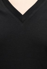 Κοντινό πλάνο στη λαιμόκοψη μαύρου πουκαμίσου V λαιμόκοψης που δείχνει λεπτομερή ραφή και ομαλή υφή υφάσματος.