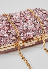 Pochette rose scintillante ornée de strass et de perles, avec une chaîne dorée et un fermoir métallique.