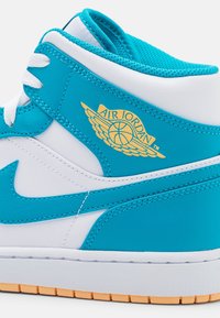 High-top sneaker with white leather and vibrant turquoise accents. Features an embossed gold "Air Jordan" logo and textured rubber sole.