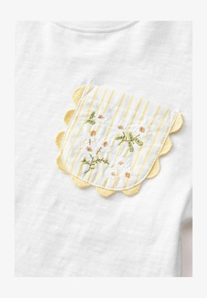 Bijela majica od tkanine s žutom džepom s udubljenim rubom, žutim vertikalnim prugama i izvezenim cvjetnim detaljima u bijeloj i zelenoj boji.